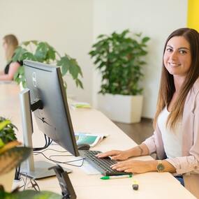 Junge Frau arbeitet am Computer im modernen Büro mit Pflanzen und freundlicher Atmosphäre.