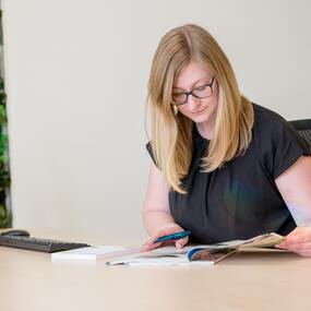 Frau mit Brille arbeitet im modernen Büro am Schreibtisch und liest konzentriert Dokumente.