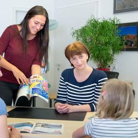 Reisebüro Beratung: Freundliche Mitarbeiterinnen zeigen einer Familie bunte Reisekataloge.