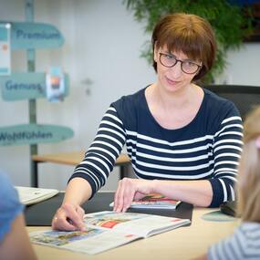 Beraterin erklärt einer Familie Reiseangebote und Urlaubsziele im Reisebüro.